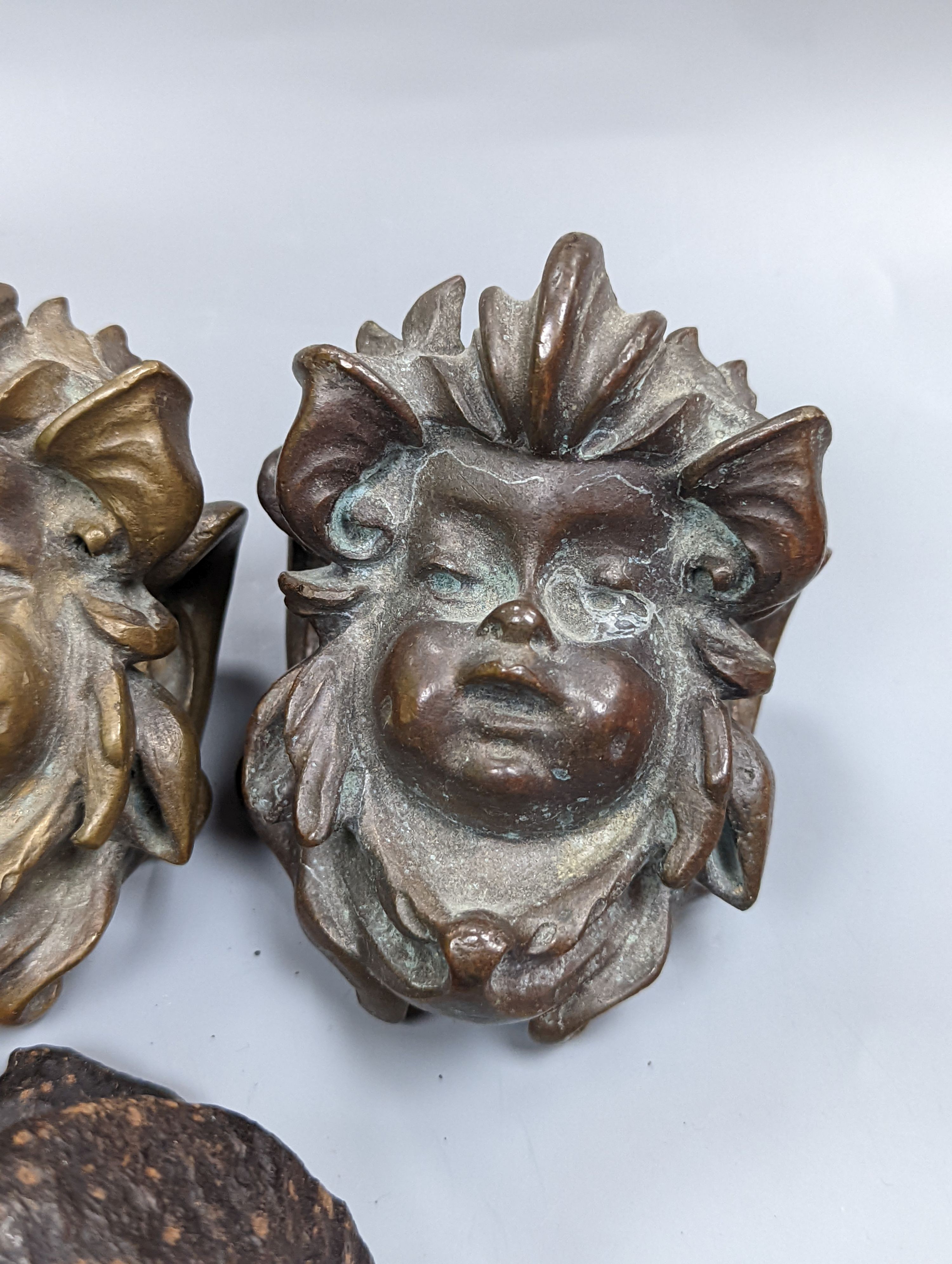 A set of three cast bronze mask-form furniture mounts, 9cm. high